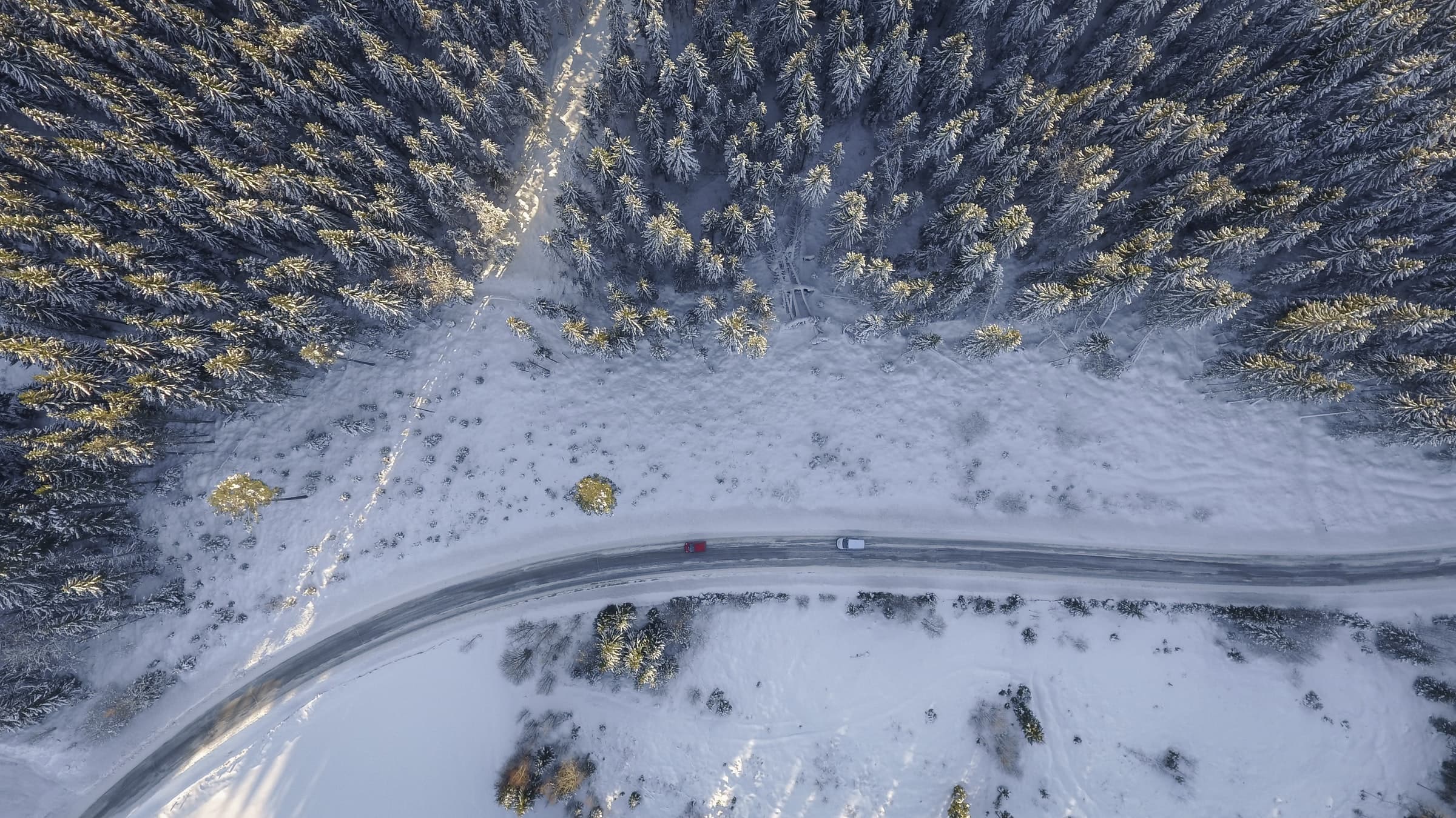 Arial view of two cars driving down a snowy, windy road